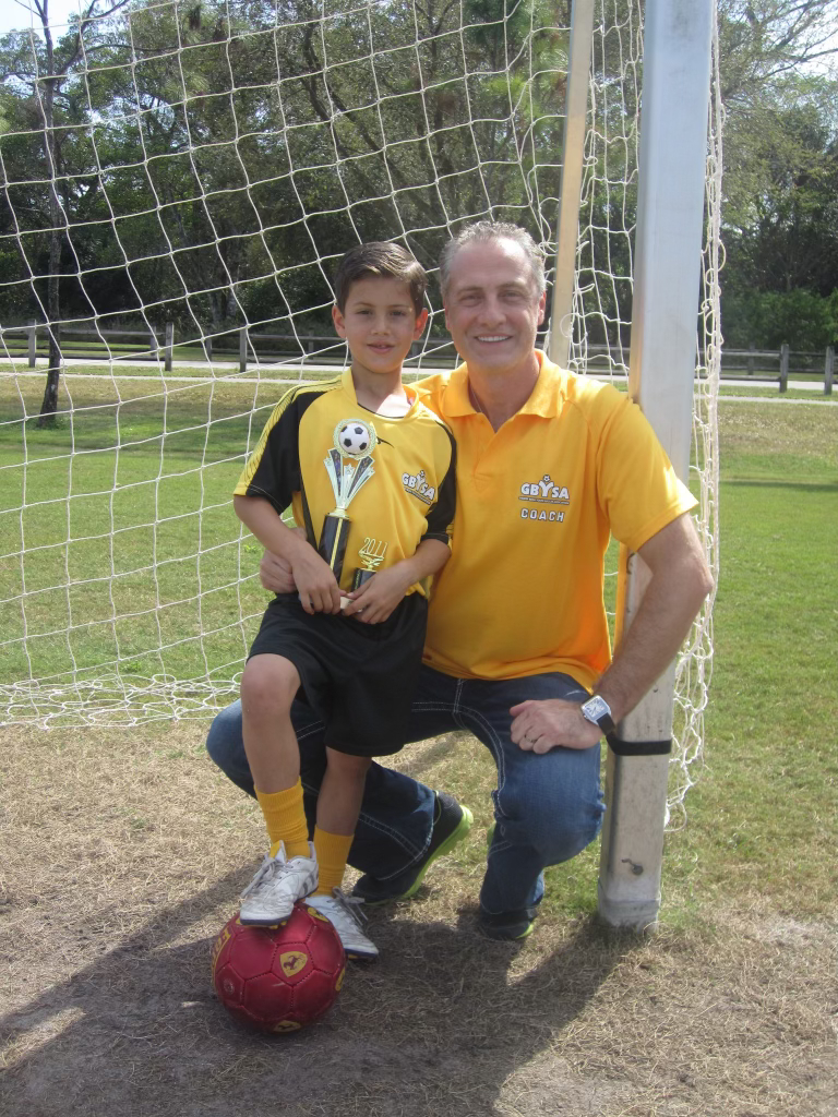 Rene, about age 8, in his soccer uniform with his dad by the goal